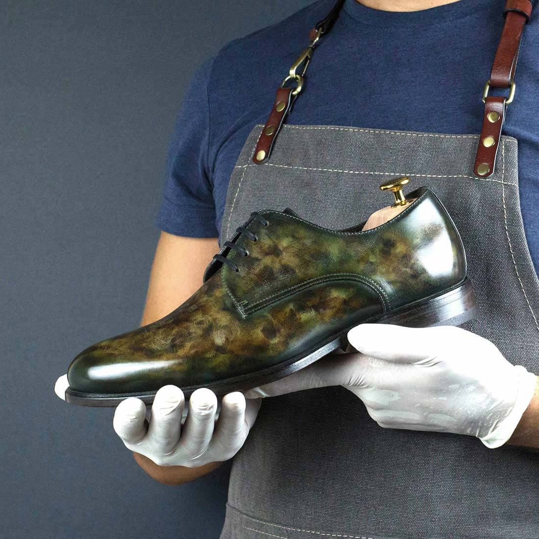 A craftsman in a denim apron, holding a luxurious hand-finished leather Luxury shoe with a unique marbled pattern, wearing white gloves to emphasize the meticulous care and quality associated with high-end shoe craftsmanship.