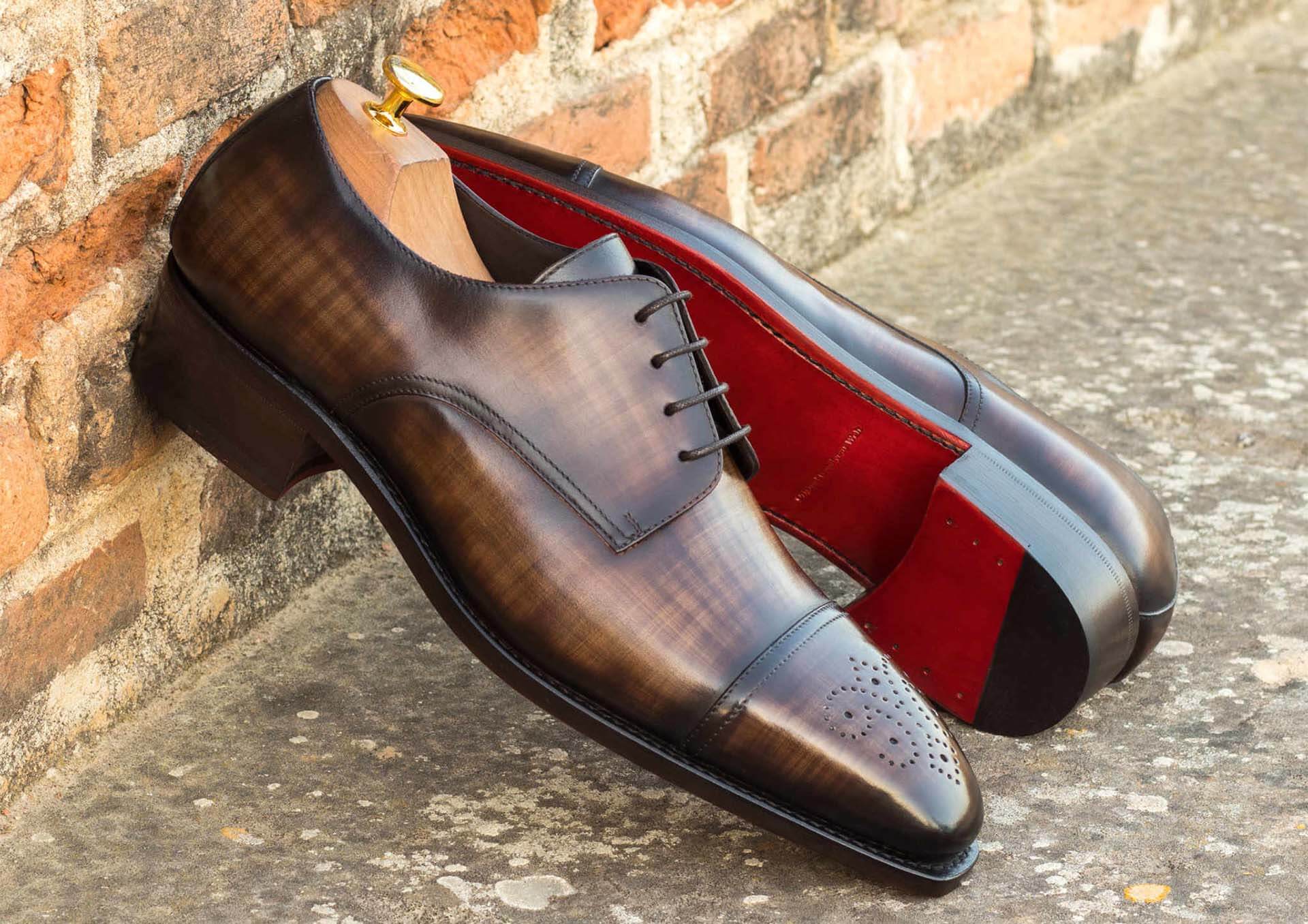 A pair of luxury shoes with polished brown leather and distinctive red soles, indicative of high-end craftsmanship, resting against a brick wall, portraying a blend of elegance and urban style.