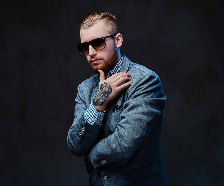 Stylish man with tattoos wearing a tailored suit and sunglasses, exuding a cool confidence and polished style.