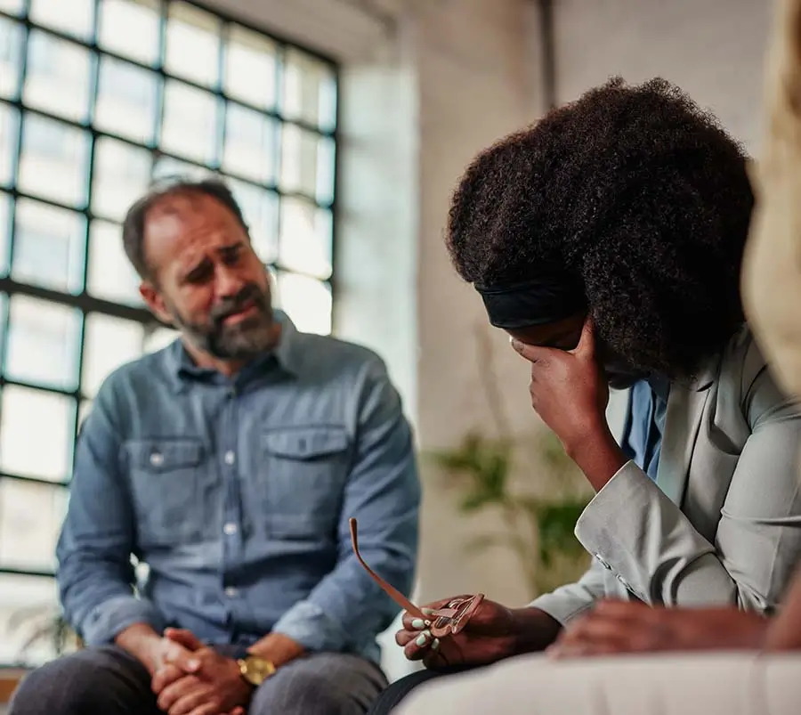 A man sitting across from a distressed African American woman holding her forehead, in what appears to be a counseling or therapy session, highlighting the importance of addressing emotional distress as part of mental health and emotional wellness.