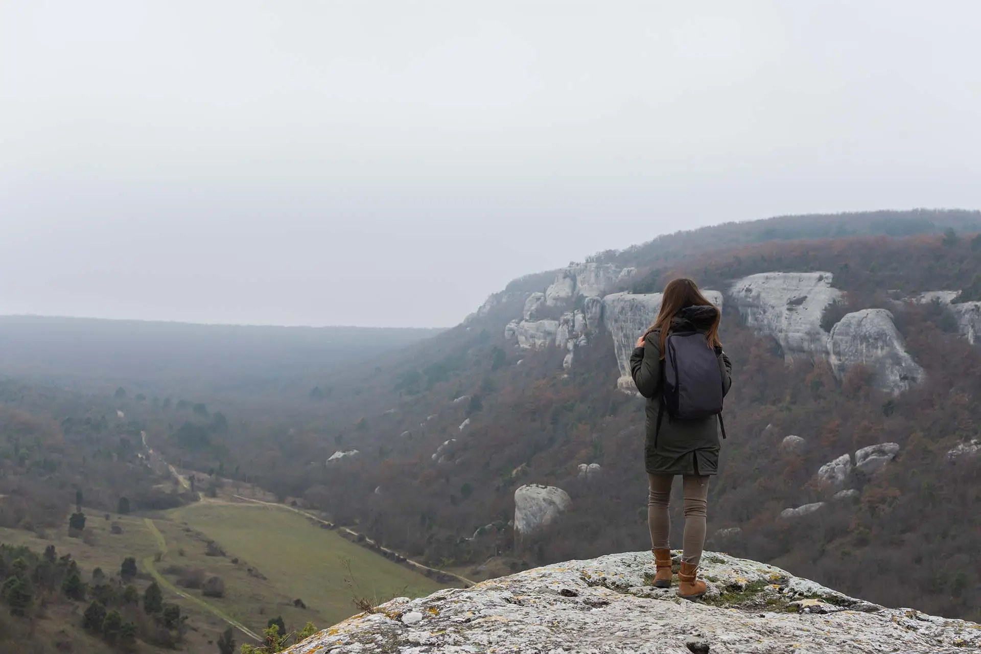 A thoughtful young woman stands on the edge of a precipice, gazing out over a vast landscape, contemplating her self-discovery for personal growth journey.
