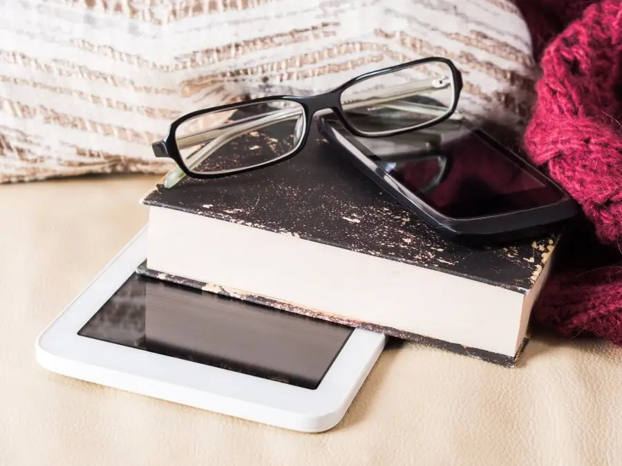 A pair of glasses rests atop a stack of books with a digital tablet and smartphone, symbolizing the integration of traditional and modern tools in lifelong learning practices.