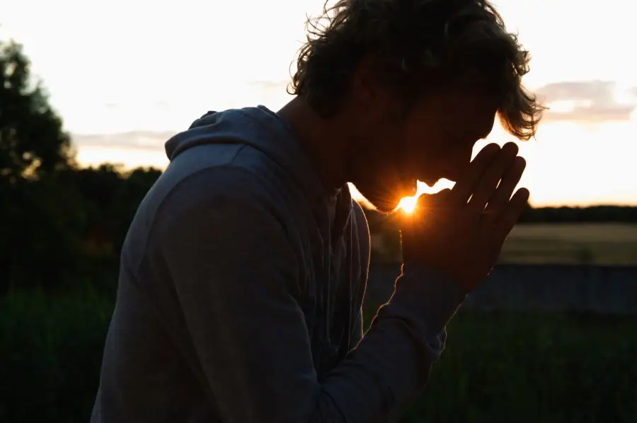 The silhouette of a man in prayer at sunset, captured in a moment of personal reflection and spiritual growth, representing the core personal growth practice of mindfulness.
