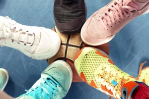 A vibrant top-down view of a circle of friends standing close together, each wearing a unique pair of sneakers ranging from classic white and pink suede to sporty black and dynamic multicolored patterns, symbolizing a collective expression of personality and self-esteem through their choice of footwear.