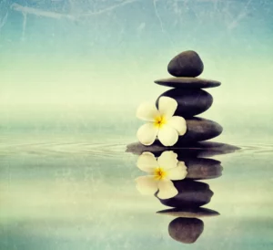 A serene stack of smooth, dark Zen stones balanced delicately with a frangipani flower on top, reflecting in the still water, symbolizing harmony, balance, and the journey towards inner peace in personal growth practices.