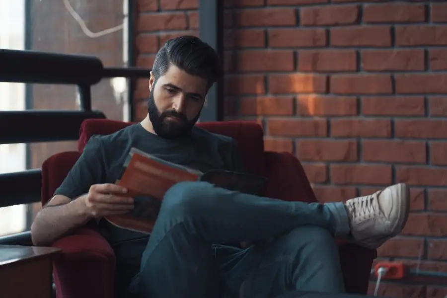 A pensive man in casual clothing engrossed in a book, embodying a relaxed yet stylish approach that aligns with cultivating confidence through personal style.